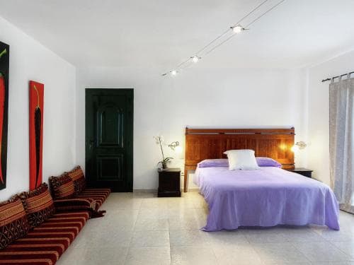 A cozy hotel room features a neatly made bed with purple linens, vibrant red artwork on white walls, and a comfortable seating area, creating a serene and inviting atmosphere ideal for travelers seeking relaxation.