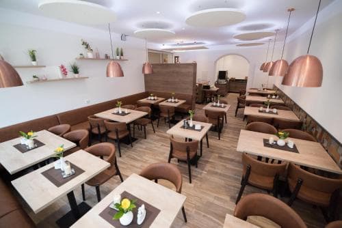 A cozy modern café with wooden tables, warm pendant lights, and neatly arranged settings invites travelers to enjoy a relaxing meal in an inviting urban dining space.