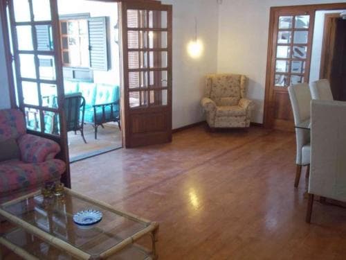 A cozy living room with wooden floors, patterned armchairs, and glass doors leading to a balcony offers a warm and inviting atmosphere ideal for a relaxing vacation rental.