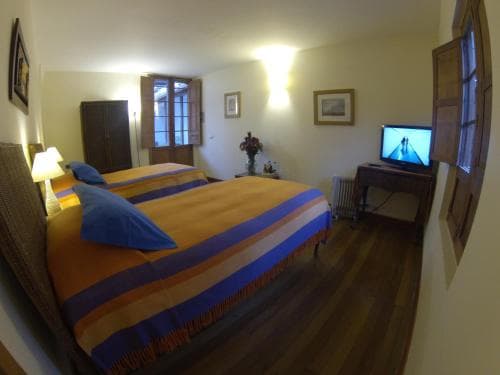 A cozy hotel room with wooden floors, two beds adorned in vibrant bedding, a small desk with a TV, and warm lighting creates an inviting atmosphere perfect for travelers seeking comfort and relaxation.