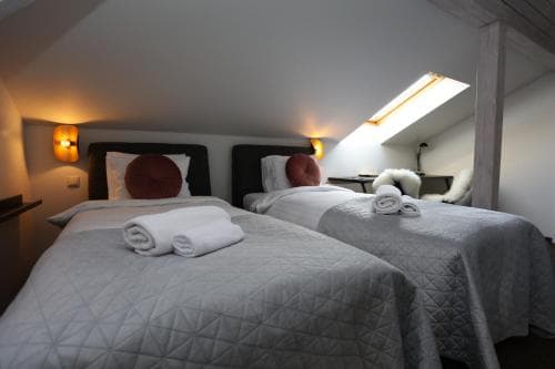 A cozy attic bedroom with two neatly made beds under slanted ceilings, illuminated by warm wall sconces, creates an inviting atmosphere ideal for travelers seeking a quaint and comfortable stay.