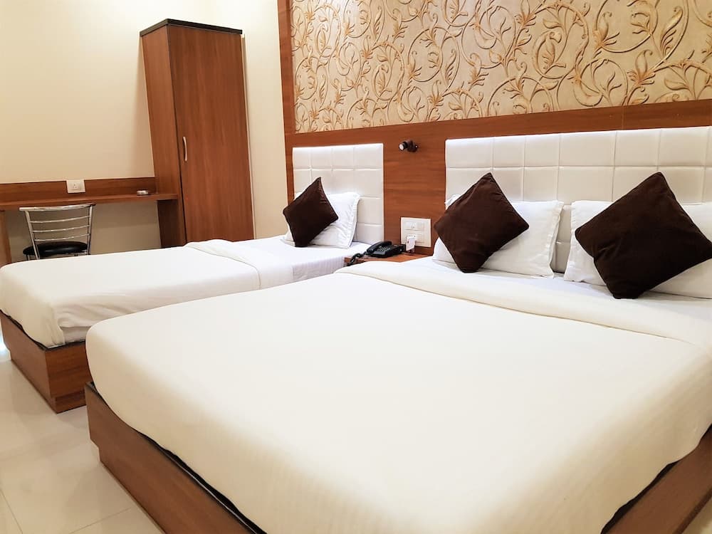 A cozy hotel room features two neatly made beds with white linens and brown pillows, a wooden wardrobe, and a desk with a chair, ideal for travelers seeking comfort and functionality.