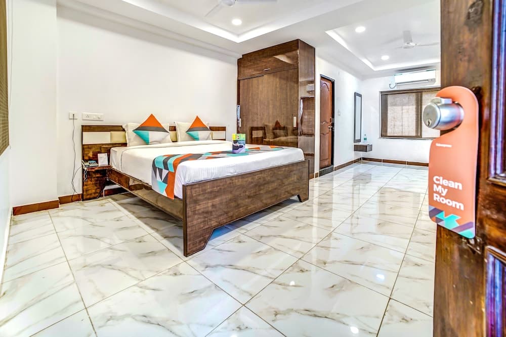 A cozy hotel room with a neatly made bed adorned with colorful pillows, marble flooring, and a "Clean My Room" sign on the door, ideal for travelers seeking comfort and cleanliness.