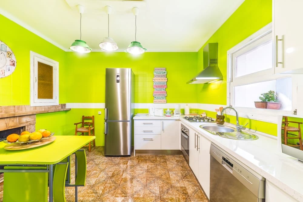 A vibrant lime-green kitchen with modern appliances, a cozy dining area, and natural light streaming through the window creates an inviting atmosphere perfect for home cooking enthusiasts.
