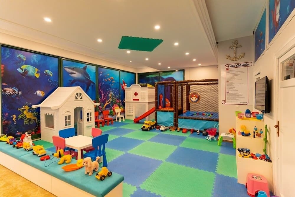 A vibrant indoor children's playroom features colorful marine-themed murals, playful furniture, and various toys, creating a cheerful and engaging environment ideal for family-friendly hotels or resorts.