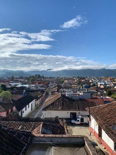 A serene rooftop view captures a charming town with tiled roofs, narrow streets, and distant mountains under a bright blue sky, ideal for travelers seeking cultural immersion and scenic vistas.