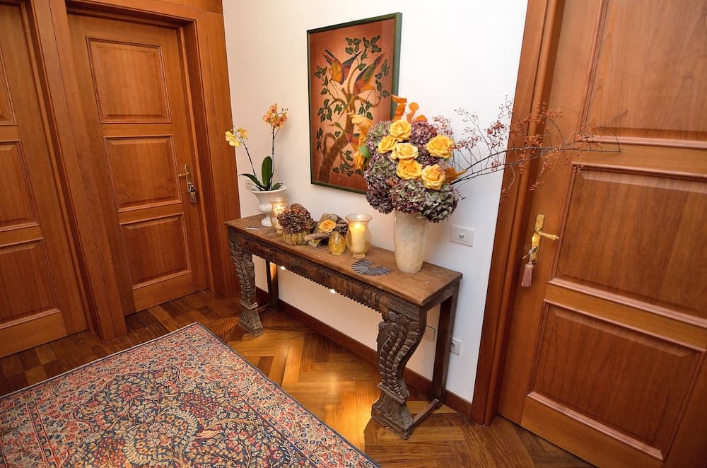 A cozy hotel entryway features a wooden console table adorned with vibrant floral arrangements and candles, framed by rich wooden doors and a patterned rug, ideal for travelers seeking warmth and elegance.