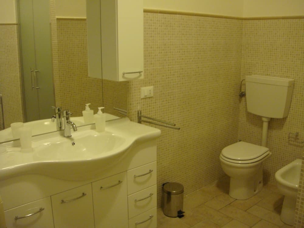A cozy bathroom with beige mosaic tiles, white fixtures including a sink, toilet, and bidet, and a sleek vanity cabinet, ideal for travelers seeking comfort and cleanliness in their accommodations.