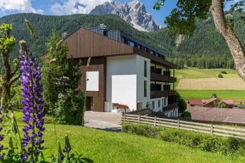A serene mountain lodge nestled in lush greenery with vibrant purple flowers in the foreground, ideal for travelers seeking a tranquil alpine retreat.