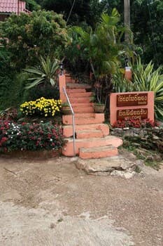 A serene tropical garden entrance features a stone staircase flanked by vibrant flowers and lush greenery, inviting travelers to explore its peaceful ambiance ideal for relaxation and photography.