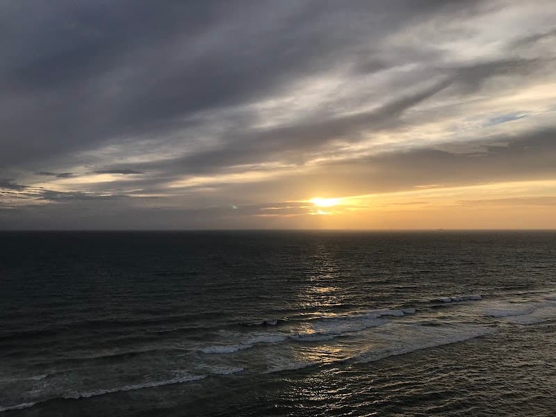 A serene sunset over the ocean with golden hues piercing through the clouds creates a tranquil mood, ideal for travelers seeking relaxation near the Radisson Hotel in Colombo, Sri Lanka.