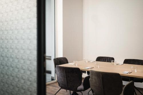 A modern conference room with sleek chairs and a polished wooden table, viewed through a patterned glass door, exudes professionalism ideal for business travelers seeking meeting spaces.
