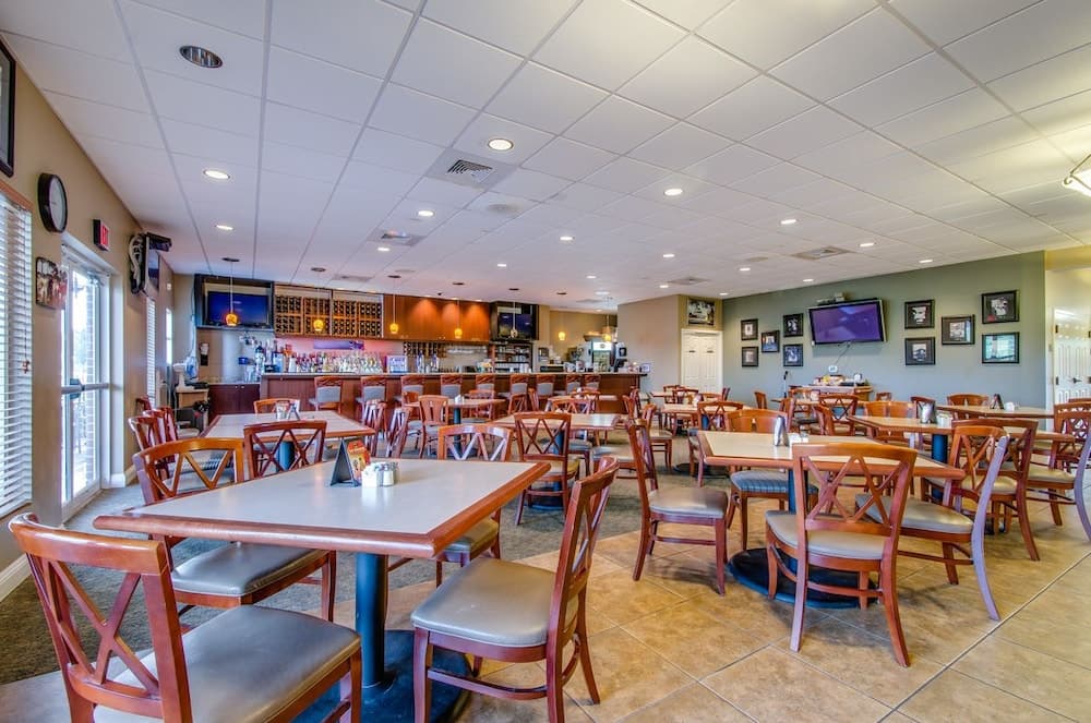 A cozy restaurant interior features wooden tables and chairs under bright ceiling lights, adorned with framed artwork on the walls, ideal for travelers seeking a comfortable dining experience.