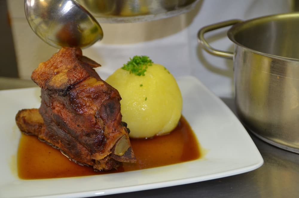 A succulent roasted pork knuckle paired with creamy potato dumpling is artfully plated in a cozy kitchen setting, perfect for culinary enthusiasts seeking traditional European cuisine experiences.