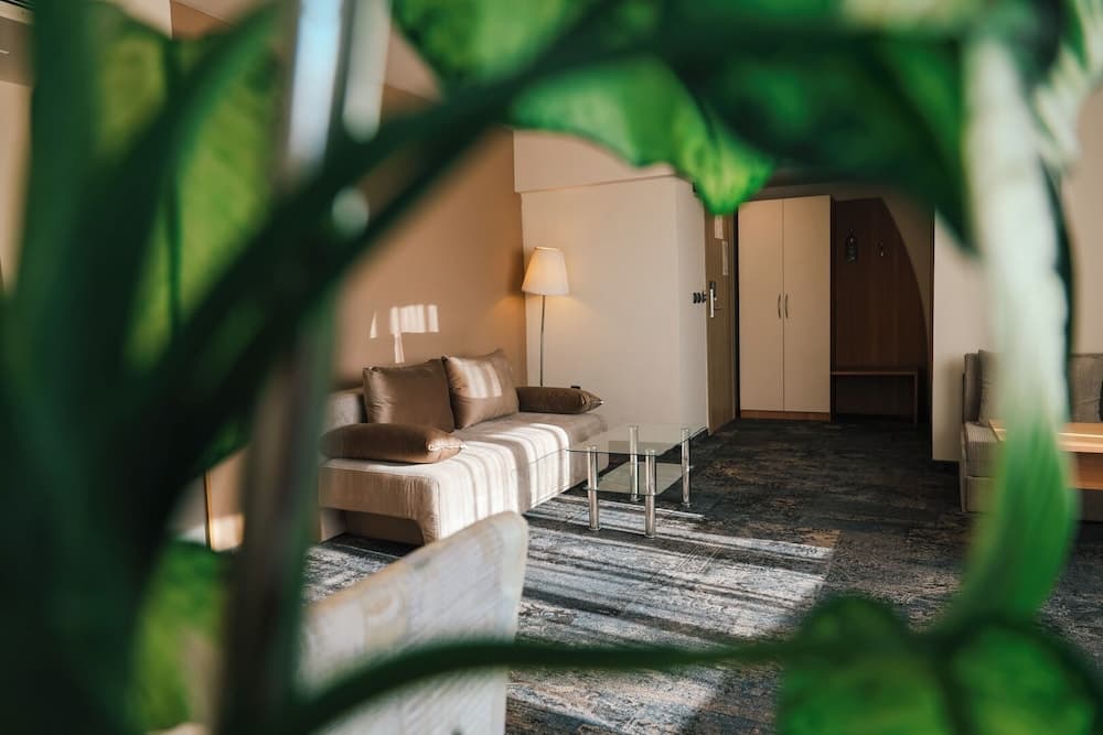 A cozy hotel room with a striped sofa, glass coffee table, and lush green plants frames the scene, inviting travelers seeking comfort and relaxation.