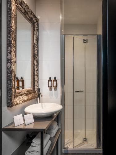 A modern bathroom features a sleek vanity with a large ornate mirror, a glass-enclosed shower, and neatly folded towels, creating a luxurious and inviting atmosphere ideal for travelers seeking comfort and style.