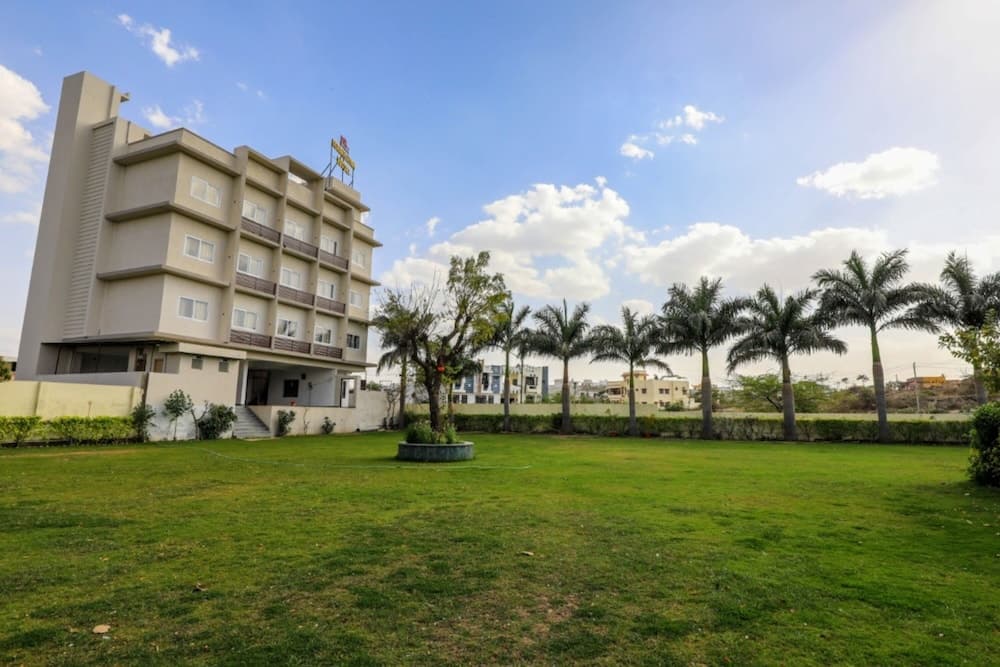 A serene hotel exterior with lush green lawns, palm trees, and a clear blue sky creates an inviting atmosphere for travelers seeking relaxation and comfort.