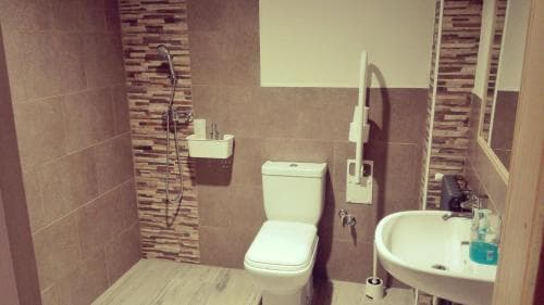 A modern, accessible bathroom with beige tiles, a wall-mounted shower, grab bars, and a sink with toiletries, ideal for travelers seeking comfort and inclusivity in accommodations.