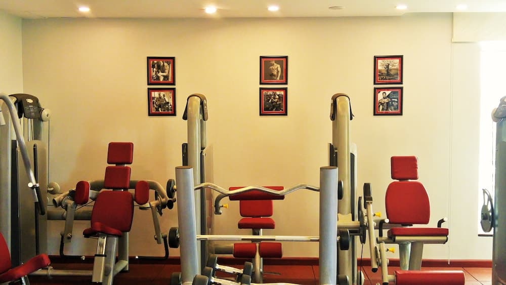 A well-lit indoor gym features red cushioned exercise machines against cream walls adorned with framed fitness posters, ideal for travelers seeking a workout-friendly accommodation.