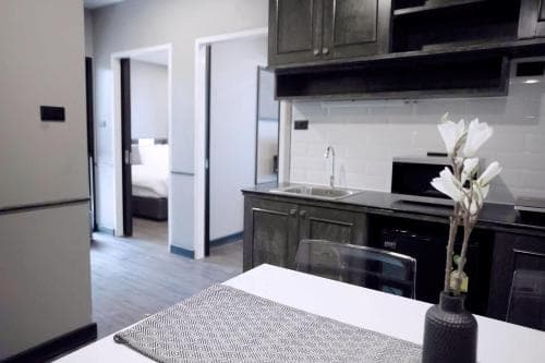 A modern apartment kitchen with sleek black cabinets, stainless steel appliances, and a dining table adorned with a vase of white flowers, creating a cozy and stylish atmosphere ideal for short-term rentals or urban living.