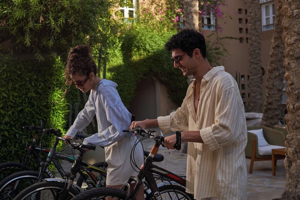 A cheerful couple prepares for a bike ride amidst lush greenery and palm trees in a serene resort courtyard, ideal for travelers seeking relaxation and outdoor activities.