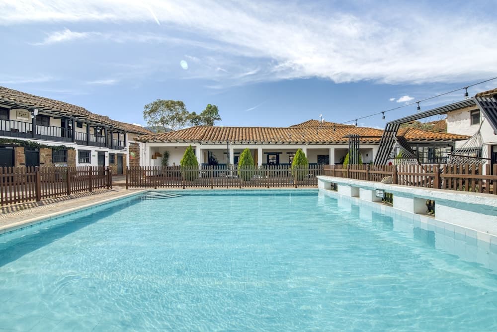 A serene resort pool surrounded by charming terracotta-roofed buildings under a bright blue sky, ideal for travelers seeking relaxation and leisure in a picturesque setting.