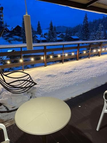 A cozy balcony adorned with string lights overlooks a serene snowy village at dusk, perfect for winter retreats and capturing the tranquil beauty of alpine landscapes.