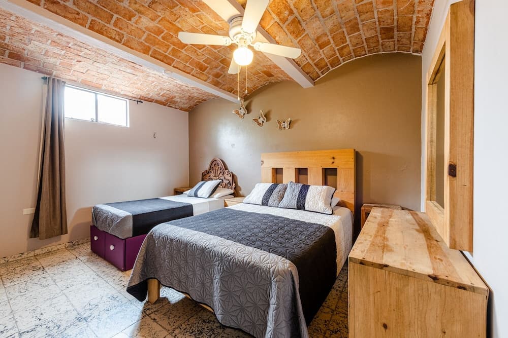 A cozy bedroom with a rustic brick ceiling, wooden furniture, and butterfly wall decorations offers a charming retreat for travelers seeking a unique and comfortable stay.