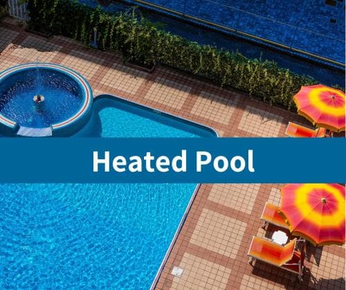 A vibrant heated pool area with crystal-clear water, colorful lounge chairs, and a striped umbrella offers a relaxing retreat, ideal for travelers seeking leisure and comfort in a resort setting.