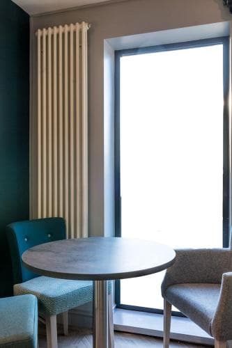 A cozy café corner features a round table flanked by plush chairs near a bright window, ideal for travelers seeking a quiet spot to relax or work.