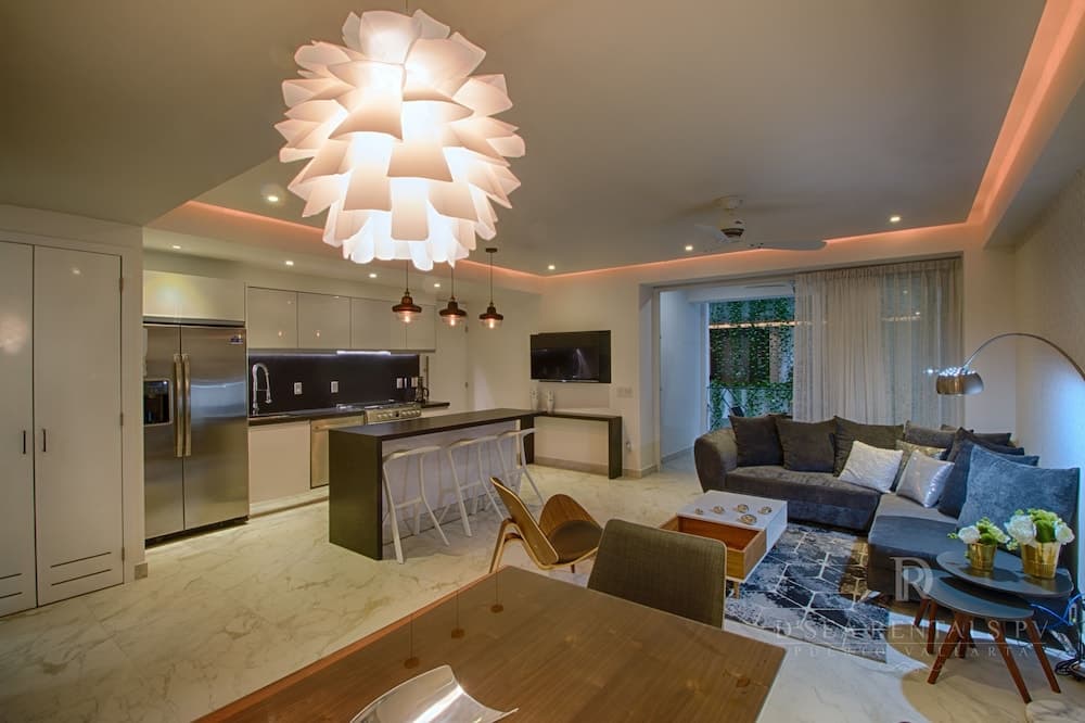 A modern, open-concept living space with sleek kitchen appliances, a cozy sofa set, and a unique flower-shaped chandelier creates an inviting atmosphere ideal for luxury vacation rentals.