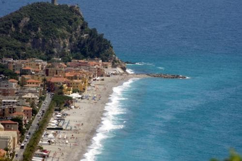 A picturesque coastal town with vibrant buildings nestled between a sandy beach and lush cliffs, offering a serene seaside escape ideal for relaxation and scenic exploration.