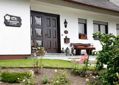 A charming white house with a welcoming entrance, lush garden, and cozy outdoor seating invites travelers seeking a peaceful rural retreat.