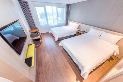 A cozy hotel room with two neatly made beds, a wall-mounted TV, and large windows letting in natural light, ideal for travelers seeking comfort and relaxation during their stay.