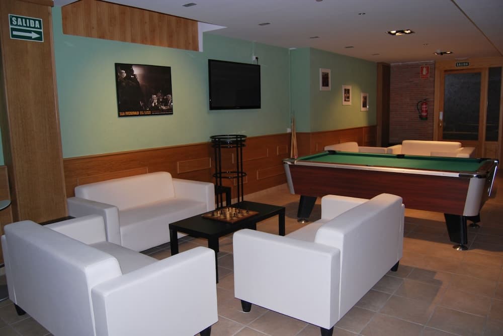 A cozy indoor lounge area features white sofas around a coffee table, a pool table, and a mounted TV, creating a relaxed atmosphere ideal for travelers seeking leisure and entertainment in a hotel or resort setting.