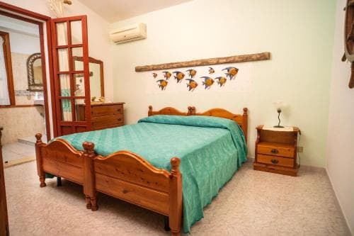 A cozy bedroom with a wooden bed adorned in teal bedding, a fish-themed wall decoration, and warm-toned furnishings creates an inviting atmosphere ideal for travelers seeking a comfortable retreat.