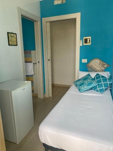 A cozy bedroom with vibrant blue walls, a neatly made bed adorned with patterned pillows, a small refrigerator, and a seashell decoration, ideal for travelers seeking a comfortable and stylish accommodation.