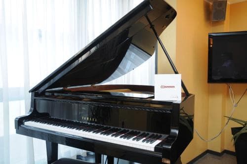 A sleek Yamaha grand piano gleams in a cozy hotel room corner, inviting travelers to unwind with music amidst soft curtains and modern amenities.