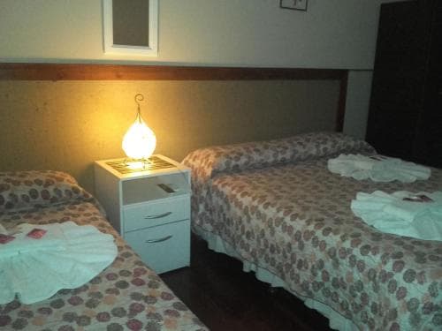 A cozy hotel room features two neatly made beds with floral bedding, a glowing bedside lamp on a small white nightstand, and a warm, inviting atmosphere ideal for travelers seeking comfort and rest.