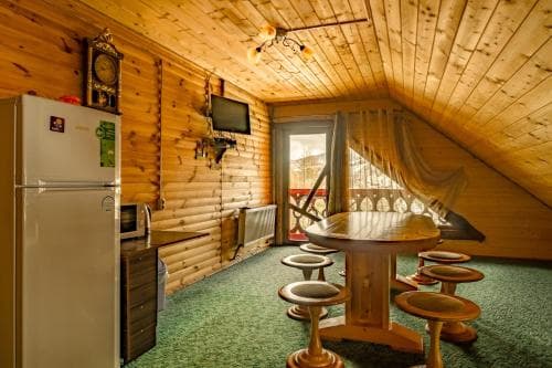 A cozy attic kitchenette with wooden walls, a round table with stools, and a balcony view, perfect for a rustic retreat or cabin getaway.