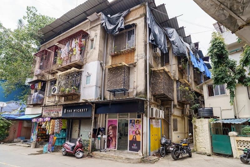 A bustling urban street in Mumbai showcases a vibrant mix of residential apartments with colorful balconies and shops at the ground level, creating a lively atmosphere ideal for cultural exploration and local shopping experiences.
