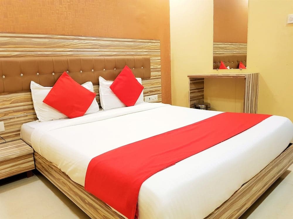 A cozy hotel room features a neatly made bed with red accents, a tufted headboard, and a small vanity area, ideal for travelers seeking comfort and simplicity.