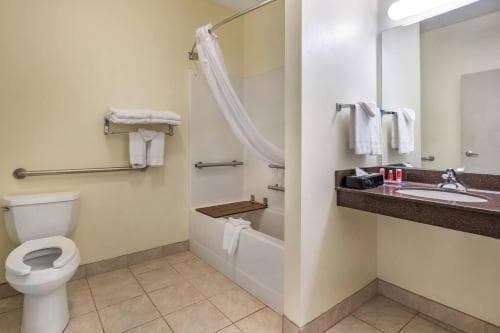 A clean, accessible hotel bathroom features a walk-in shower with a bench, grab bars, a toilet, and a sink with toiletries, ideal for travelers seeking comfort and convenience.