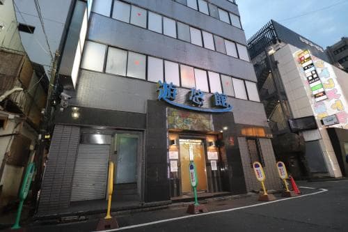 A quiet urban street at dusk showcases a multi-story building with illuminated signage in Japanese characters, evoking a calm yet vibrant city atmosphere ideal for exploring nightlife or local businesses.