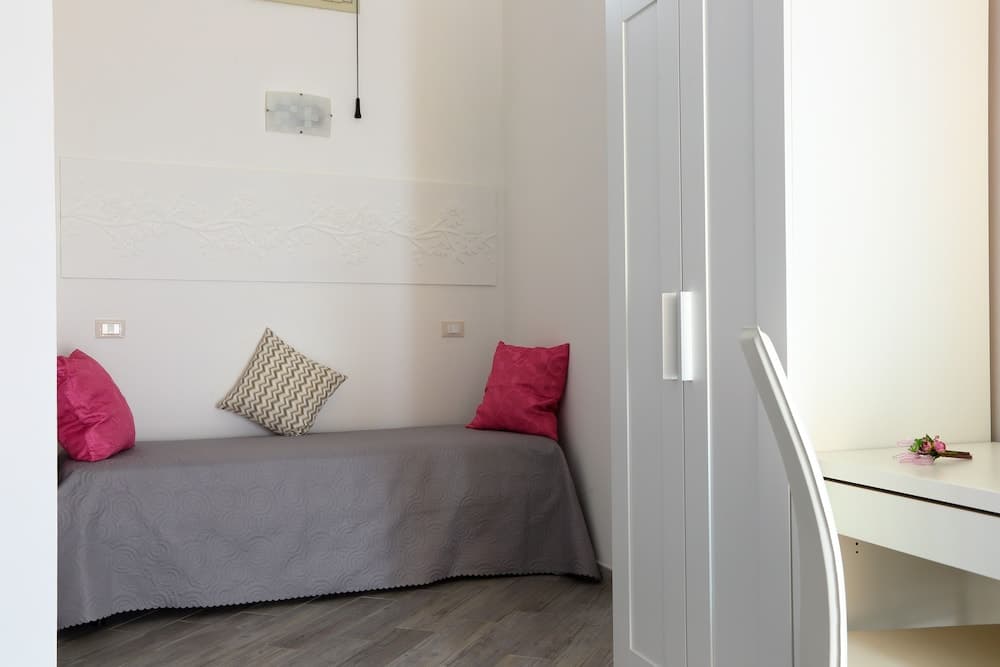 A cozy bedroom with a neatly made bed adorned with pink and patterned pillows, white cabinetry, and a sleek desk, ideal for travelers seeking a comfortable and stylish accommodation.