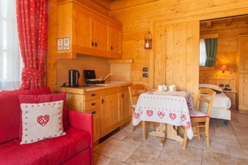 A cozy wooden cabin interior featuring a red sofa, heart-patterned cushions, a small dining table, and warm lighting, ideal for a romantic getaway or family vacation in a rustic mountain retreat.