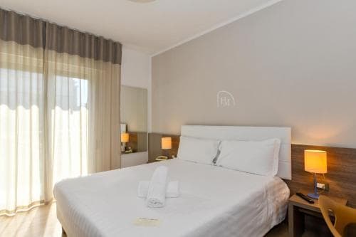 A cozy hotel room with a neatly made bed, soft lighting from bedside lamps, and large windows draped with elegant curtains, ideal for travelers seeking comfort and relaxation.