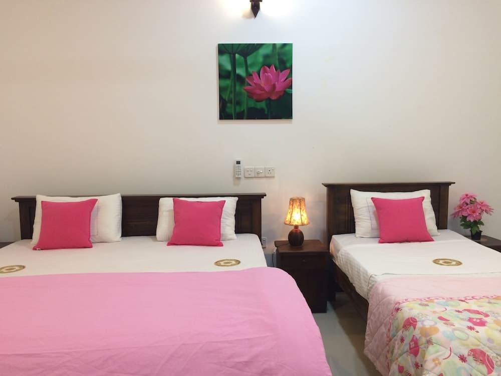 A cozy hotel room features two neatly made beds adorned with pink bedding, a warm-toned lamp on a wooden nightstand, and a vibrant lotus flower painting, ideal for travelers seeking comfort and tranquility.