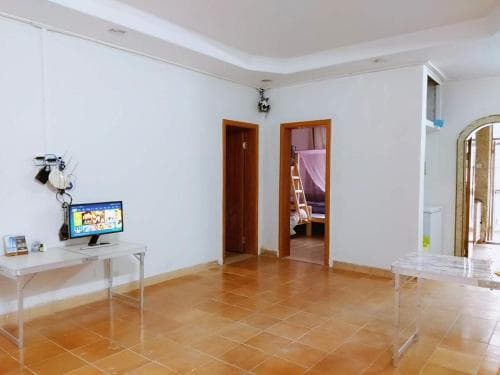 A cozy apartment interior features tiled floors, wooden doors leading to other rooms, a desk with a computer displaying vibrant colors, and a serene atmosphere ideal for travelers seeking a quiet stay.