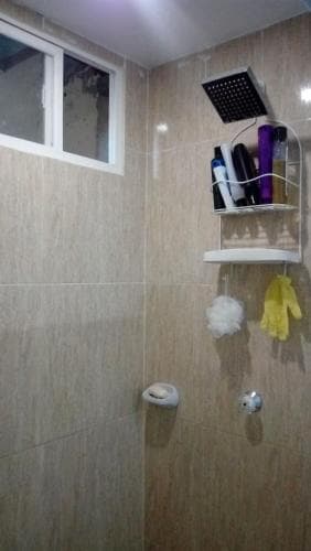 A cozy bathroom with beige tiled walls features a mounted showerhead, toiletries on a shelf, and a window, ideal for travelers seeking a clean and functional space.